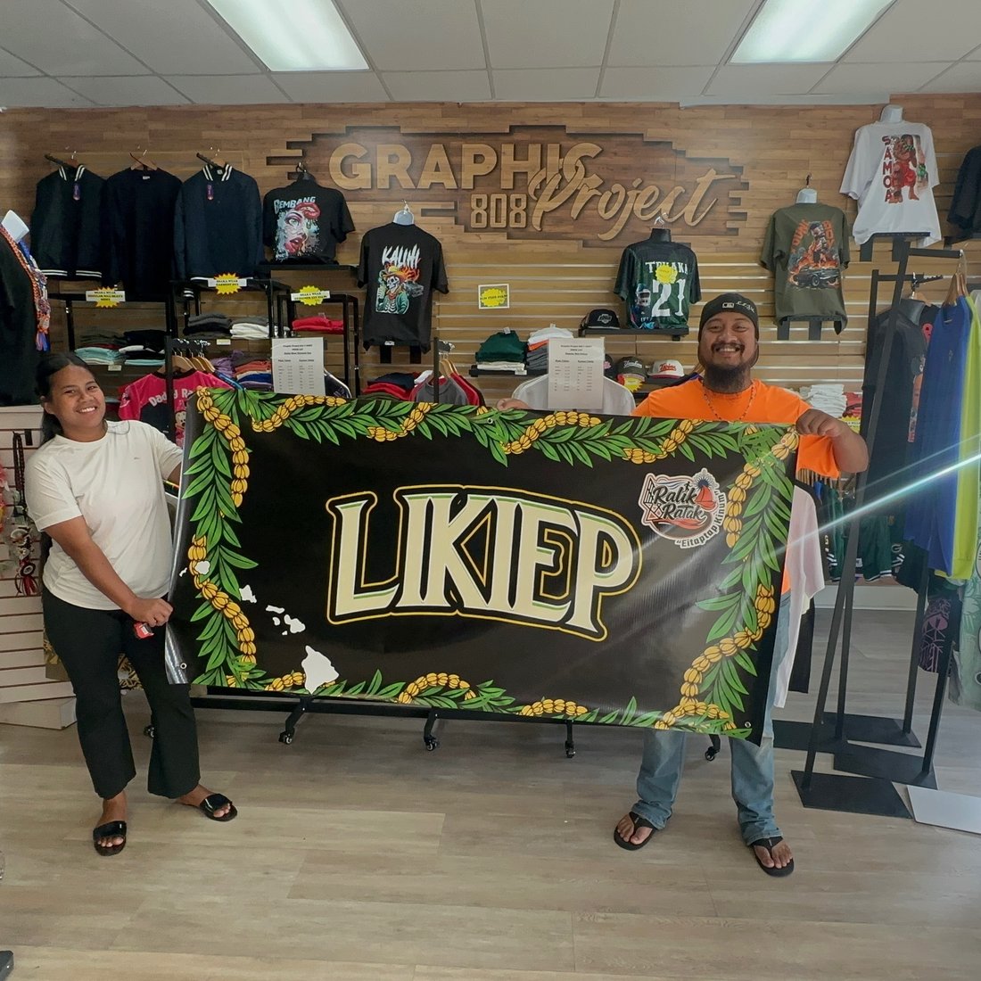 Two customers holding a custom Likiep banner made at Graphic Project 808